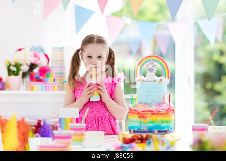 Kids birthday party with colorful pastel decoration and unicorn rainbow cake. Little girl with sweets, candy and fruit. Balloons and banner at festive Stock Photo