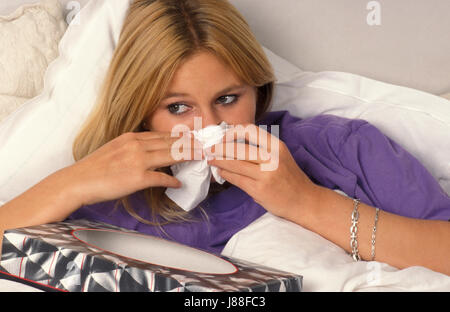 young woman in bed blowing her nose on tissue