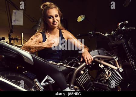 Blond woman mechanic showing thumbs up in a motorcycle workshop Stock Photo