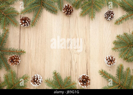 Christmas frame out of fir tree twigs and snowy pine cones on brown wooden background with lots of copy space. Stock Photo