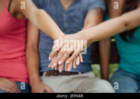 Young teenagers sitting on a wooden bench and stacking hands, friendship and cooperation concept Stock Photo