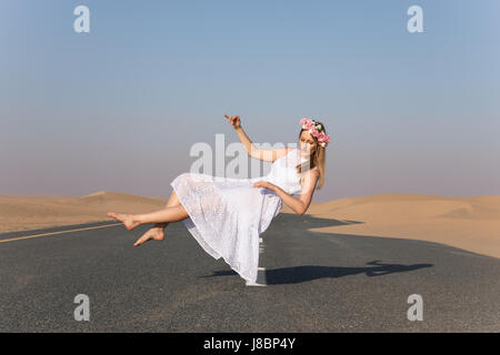 Young beautiful girl with blonde hair and flower crown floating in the air in the desert. Stock Photo