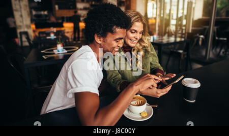 Shot of happy young man with his female friend sitting together at cafe and using mobile phone. Best friends at coffee shop looking at smart phone. Stock Photo