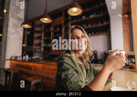 Portrait of beautiful young woman sitting at cafe with cup of coffee and smiling. Caucasian female having coffee at cafe. Stock Photo