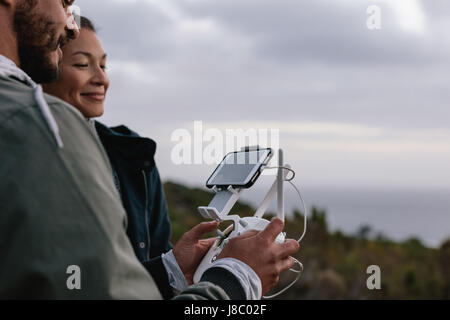 Couple using aerial drone for photography. Man and woman standing in countryside taking photo on flying drone during vacation. Stock Photo