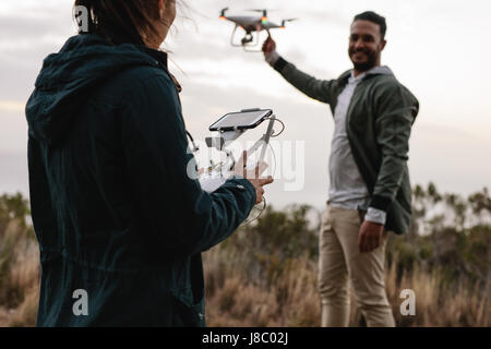 Woman with remote control and  man holding a flying drone in countryside. Young couple flying drone in countryside. Stock Photo