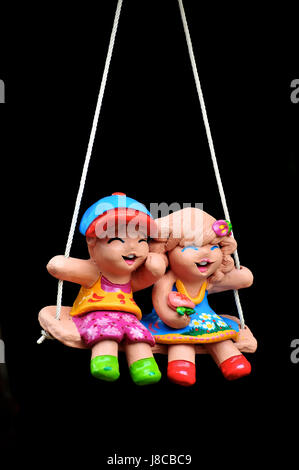 Earthernware child doll on the swing used for garden decoration. Stock Photo