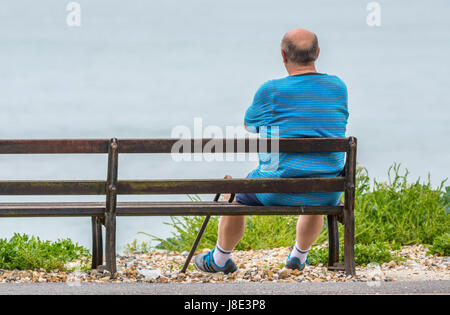 A man sitting alone on a bench while looking out to sea, in the UK. Stock Photo