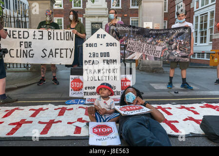 May 26, 2017 - London, UK - London UK. 26th May 2017. A father poses with the son he carries on his bicycle in front of the tombstone at the Stop Killing Cyclists protest vigil and die in outside the Tory Party HQ to mark the deaths of an estimated 280,000 people from air pollution, largely transport related and a further estimated 168,000 people from inactivity diseases due to lack of protected cycle lanes, since the Tories were elected in 2017. They demand that 10% of the transport budget be spent on clean-air protected cycling infrastructure by 2020. A similar protest took place outside the Stock Photo