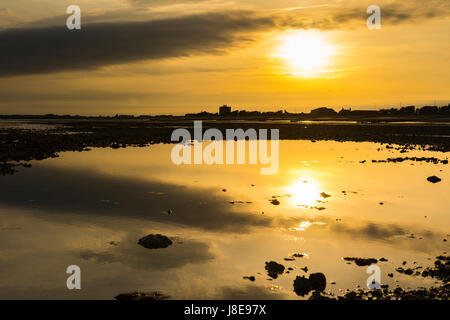 Reflections of a low sun in remaining water at low tide on a beach in the UK. Stock Photo