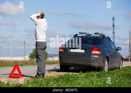 Man stands on road near broken car in afternoon Stock Photo