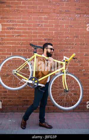 Bearded man with a fixie bicycle. Confident bearded man carrying his bicycle on shoulder and looking at camera while walking outdoors. Stock Photo