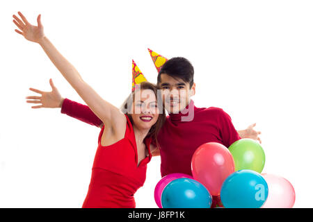 Young happy woman with long chestnut hair in red dress and young smartlooking man in red shirt with celebrating hats holding many colored balloons on  Stock Photo