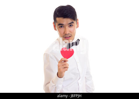 Nice man with black hair in white T-shirt with black bow-tie holding a red paper heart on white background in studio Stock Photo
