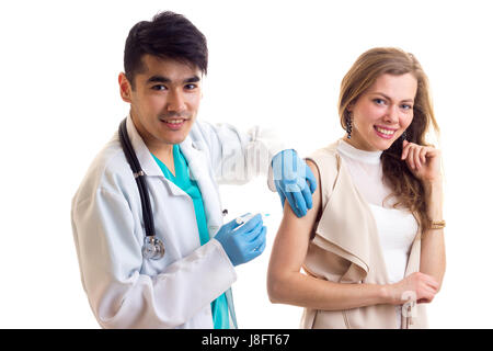 Young smartlooking doctor with dark hair in white gown with stethoscope and blue gloves making an injection of young smiling woman with long brown hai Stock Photo