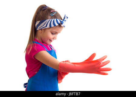 Beautiful little girl with ponytail wearing in pink shirt and blue apron with red gloves on white background in studio Stock Photo