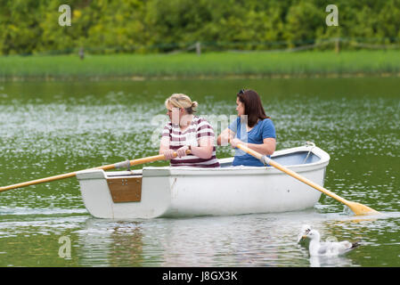 Female friends in a small wooden rowing boat on a boating lake in Spring. Stock Photo