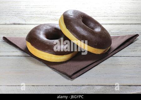 chocolate iced donuts with napkin on wooden background Stock Photo