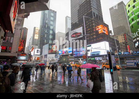 people holding umbrellas walk through wet times square during rain shower midtown New York City USA Stock Photo