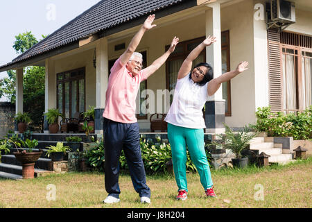 Active senior couple exercising with raised arms outdoors Stock Photo