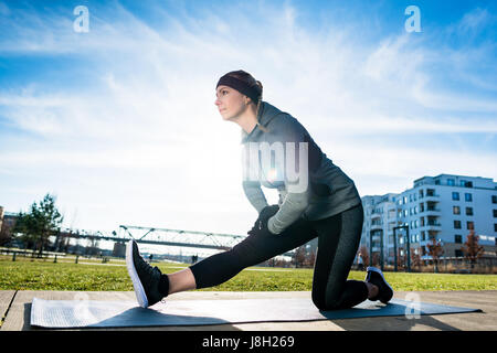Determined young woman stretching her leg while kneeling on a ma Stock Photo