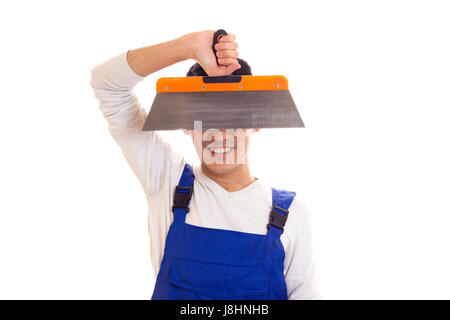 Young funny man with black hair in white shirt and blue overall holding spatula on white background in studio Stock Photo