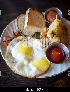 Two sunny side up eggs, hash brown potatoes, sourdough toast, and bacon (Canadian breakfast) from Chartier Restaurant in Beaumont, Alberta, Canada. Stock Photo