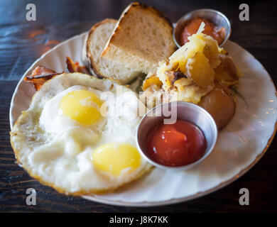 Two sunny side up eggs, hash brown potatoes, sourdough toast, and bacon (Canadian breakfast) from Chartier Restaurant in Beaumont, Alberta, Canada. Stock Photo