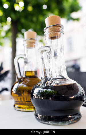 Bright yellow olive oil and black balsamic vinegar on the restaurant kitchen table. Two bottles foreground. Bottling of dressing. Stock Photo