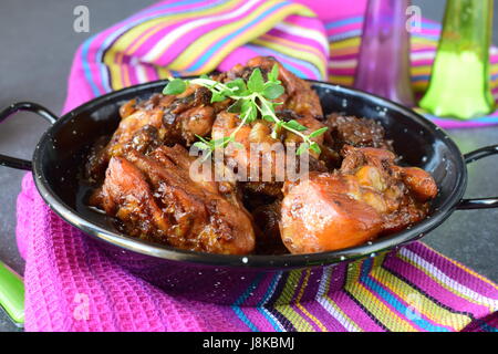 Chicken with prunes cooked in the oven in a black bowl on a textile background. Stock Photo