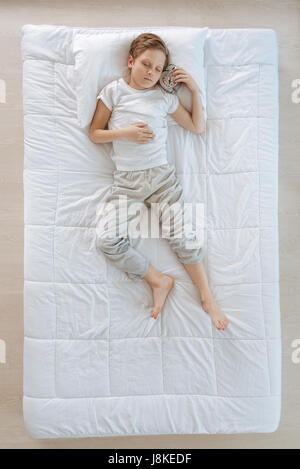 Time to wake up. Sleepy nice cute boy holding an alarm clock and listening to it while having a nap Stock Photo