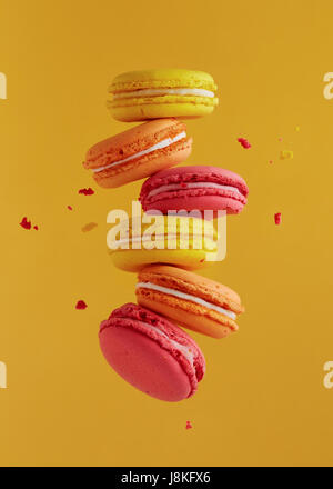 Different types of macaroons in motion falling on yellow background. Sweet and colourful french macaroons falling or flying in motion. Stock Photo