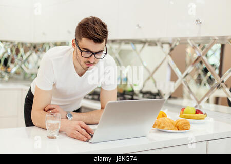 Young bearded businessman wearing white T-shirt, using laptop. Man checks email on computer. Freelancer working outside office Stock Photo