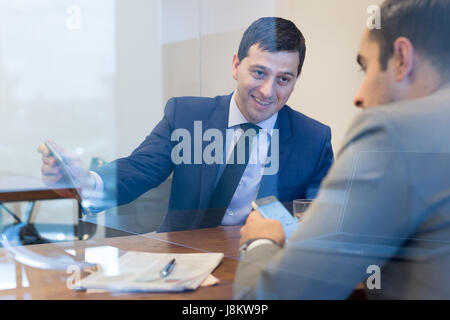Two businessmen using smart phones and touchpad at meeting. Stock Photo