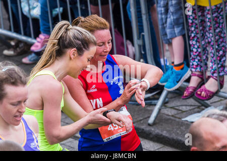 Two women cross the finishing line of the 2017 Liverpool Rock n Roll half marathon and immediately pause to check their finishing times on their watch Stock Photo