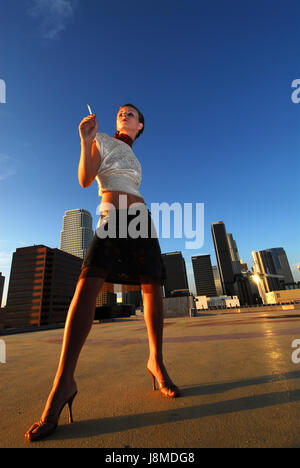 Portrait of young fashion woman posing In elegant dress on rooftop with a view the city of Los Angeles Stock Photo