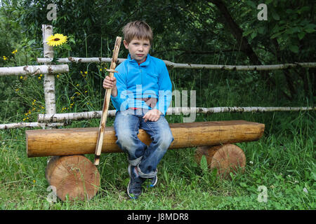 Boy with wooden sword sitting on log bench Stock Photo