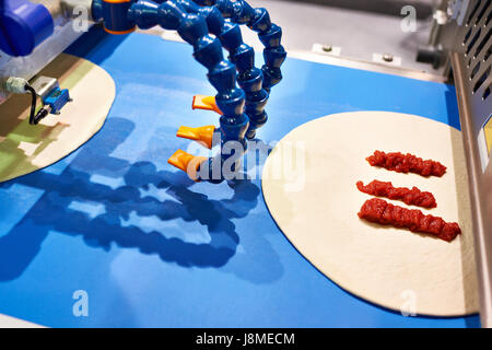 Device for adding tomato sauce to pizza on the conveyor Stock Photo