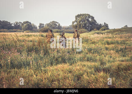 Group of hunters crossing through tall grass in rural field at dawn during hunting season Stock Photo