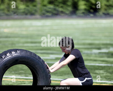 Close up of teen age girl pushing large tire on sports field to build strength Stock Photo