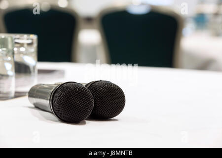 Two microphones on a white table used for Q&A at a conference or meeting venue. Chairs and a screen in the background Stock Photo
