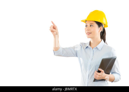 smiling woman builder in safety helmet with pad computer and pointing air copyspace pressing virtual image area on white wall. concept of repair build Stock Photo