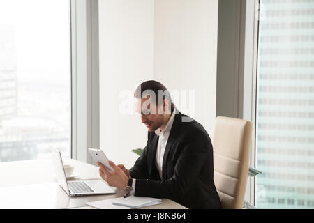 Entrepreneur using digital tablet while sitting at desk in office. Executive manager browsing online with phablet, watching video online. Businessman Stock Photo