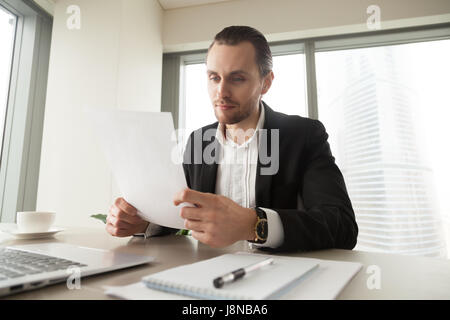 Successful businessman examines company financial documents at desk in office. Young entrepreneur reading contract at workplace. Executive manager ana Stock Photo
