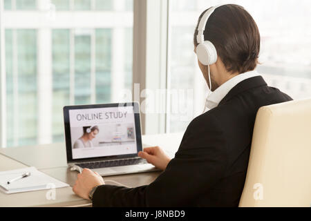 Man in headphones at of laptop with online study service web page on screen. Office worker chooses free online qualification training course, improvin Stock Photo