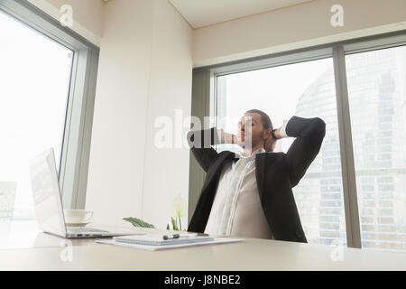 Satisfied happy man leaning back in chair hands behind head in office. Successful entrepreneur enjoys good work, dreams about future at workplace. Off Stock Photo
