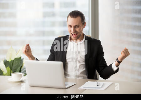 Happy businessman excited because of great deal, achievement, company success. Young entrepreneur screaming with joy while looking on laptop screen. M Stock Photo