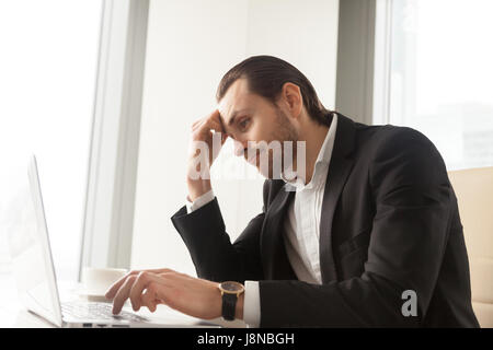 Young businessman at desk tired from routine laptop work. Entrepreneur boring at workplace, sick of monotonous work. Office worker procrastinates whil Stock Photo
