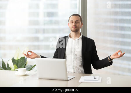 Relaxed corporate man sitting with closed eyes contemplating at work desk with laptop in office. Guy relaxing, relieves stress, gets positive thinking Stock Photo