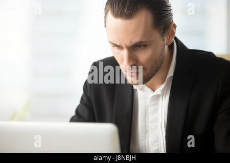 Focused businessman looking on laptop screen. Serious financier reviewing financial market fluctuations. Entrepreneur immersed in work on computer. Yo Stock Photo